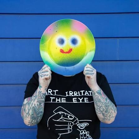 Person hält einen farbenfrohen Melamin-Teller von Jon Burgerman mit lächelndem Gesichtsmotiv vor das Gesicht